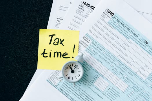 pexels-photo-6863259-6863259-1 A stack of tax forms with a clock and yellow sticky note saying 'Tax time!' indicating urgency.